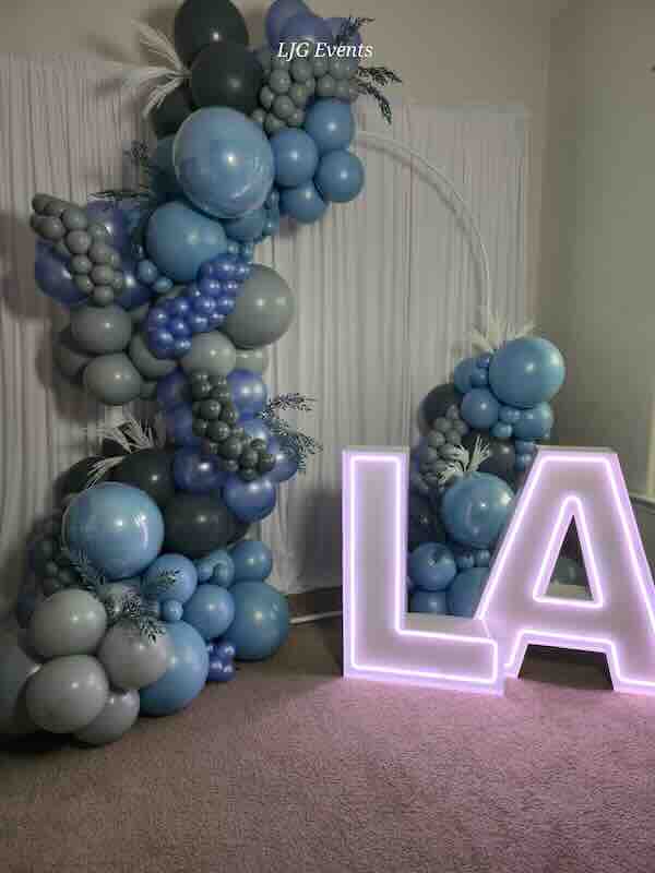 Blue and gray balloon arch with neon letters.