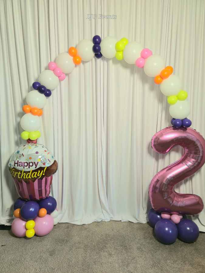 Colorful balloon arch with cupcake and number two.