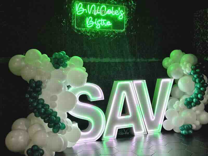 Neon-lit bistro sign with SAV letters and balloons.