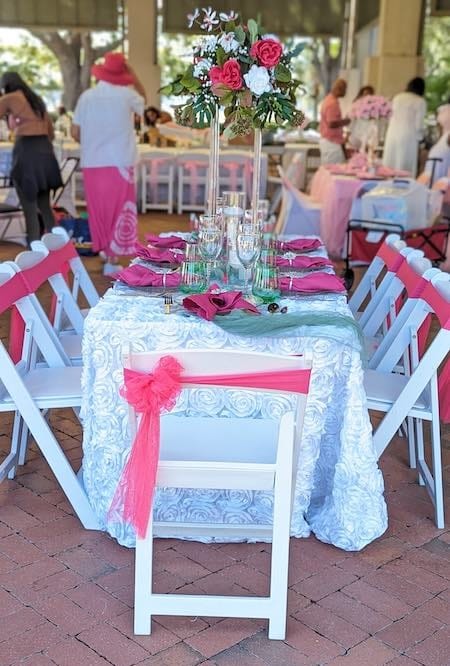 Pink ribbons on chairs at a table for an event.