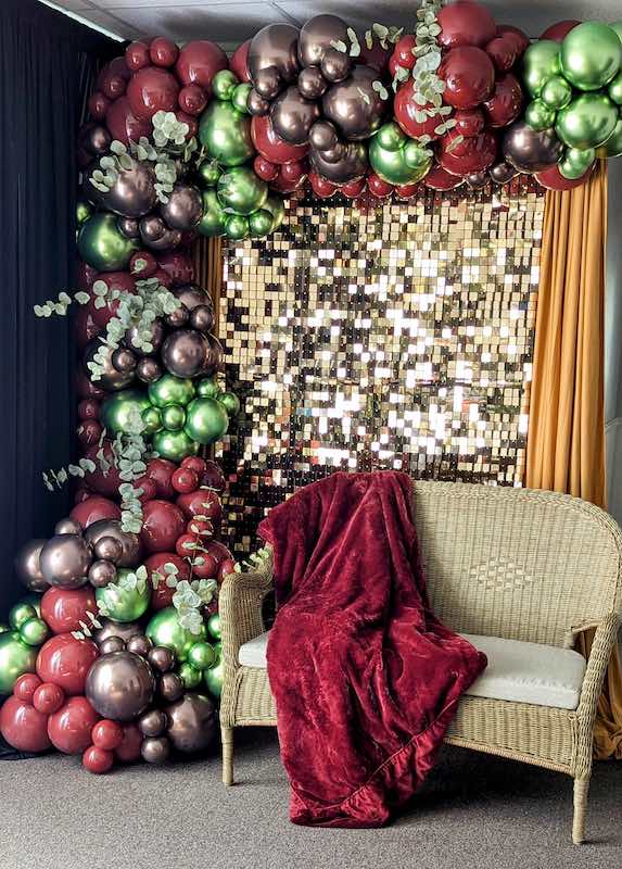 A beautiful burgundy, purple, and green balloon garland behind a loveseat.