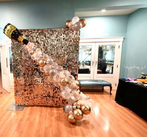 Champagne-themed balloon decor with sequin backdrop display.