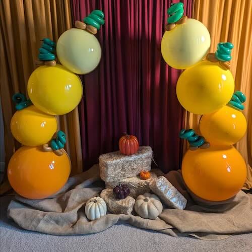Colorful balloon arch with pumpkins for fall decor.