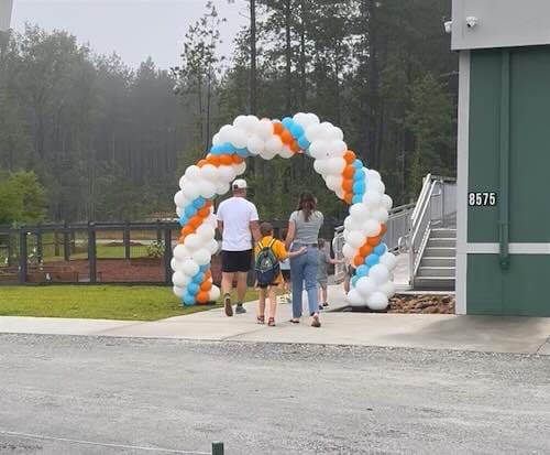 Family walking under colorful balloon arch outdoors.