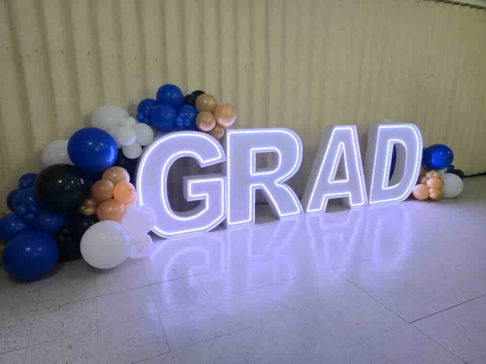 Illuminated GRAD letters surrounded by blue and white balloons