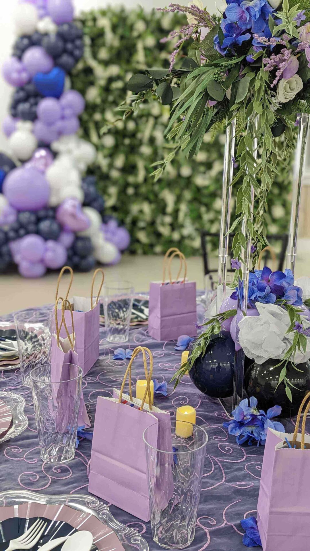 A beautiful purple and blue decorated table with a balloon wall behind it.
