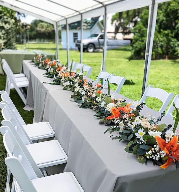 A wedding table set with floral settings inside of a tent outside in the daytime.